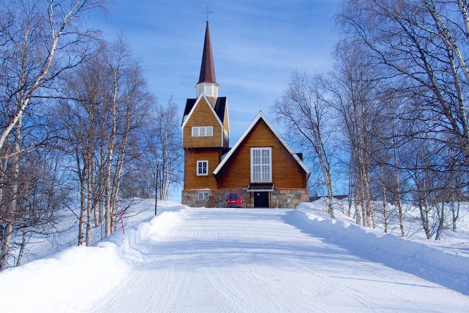 Una iglesia de madera con un campanario alto rodeada de árboles cubiertos de nieve.