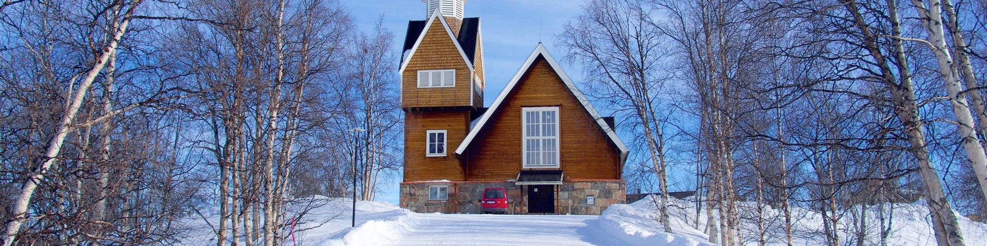 Una iglesia de madera con un campanario alto rodeada de árboles cubiertos de nieve.