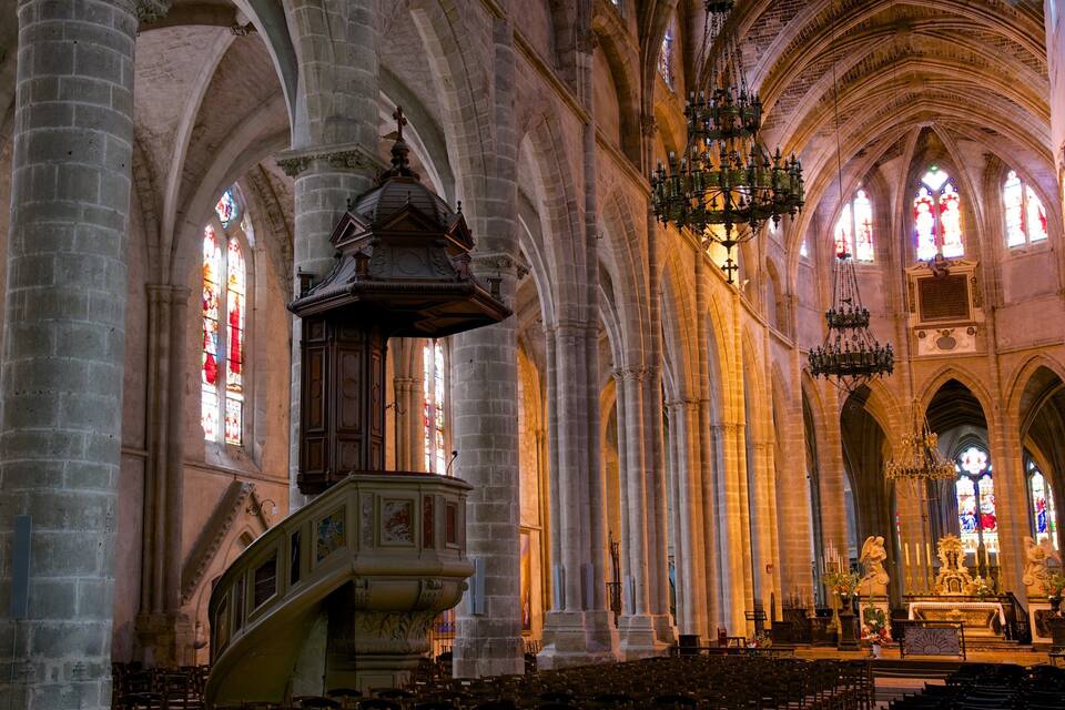 L’intérieur d’une cathédrale, avec ses voûtes en arc, ses vitraux et son clocher central.
