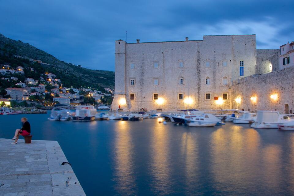 A harbor with boats, a stone building, and a person sitting on a ledge.