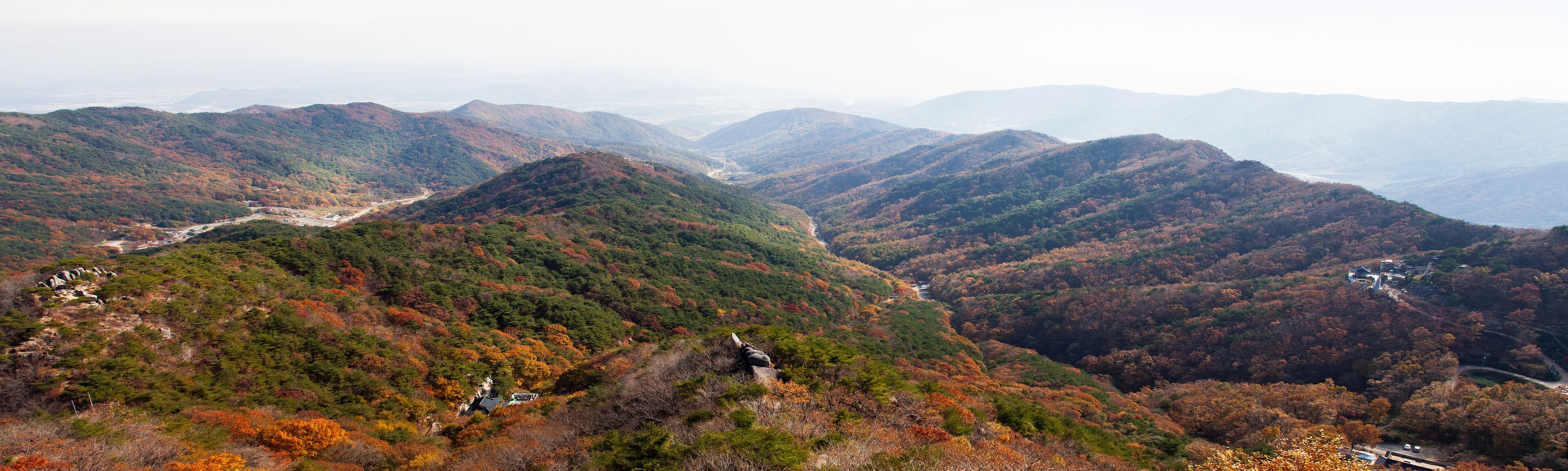 A mountainous landscape with autumn foliage, a winding road, and a small building.