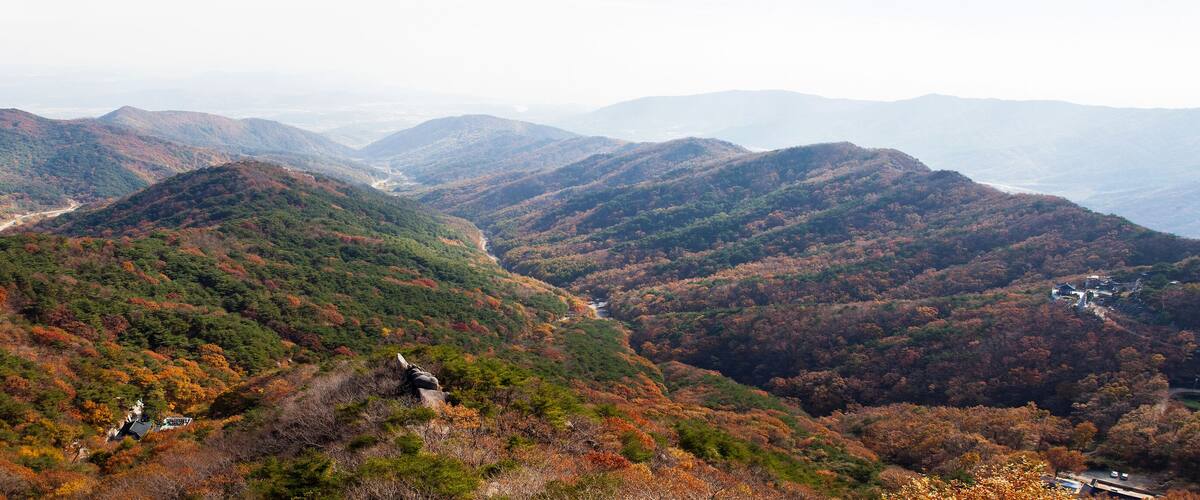 A mountainous landscape with autumn foliage, a winding road, and a small building.