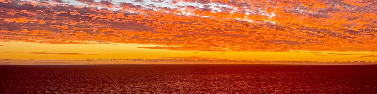 A sunset over a body of water with a sky filled with clouds.