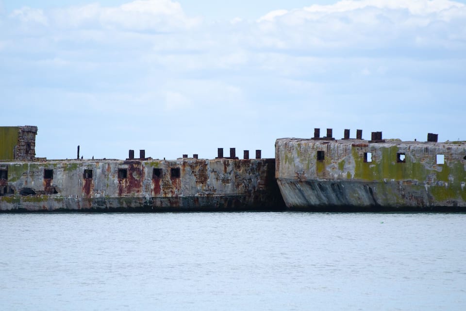 A weathered, rusted pier with multiple rusted bollards and a partially intact structure.