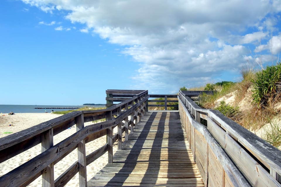 A wooden boardwalk leading to a beach with a sandy shore and dunes.