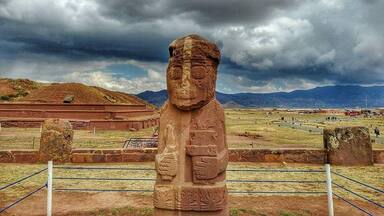 A stone statue in a field with mountains in the background.