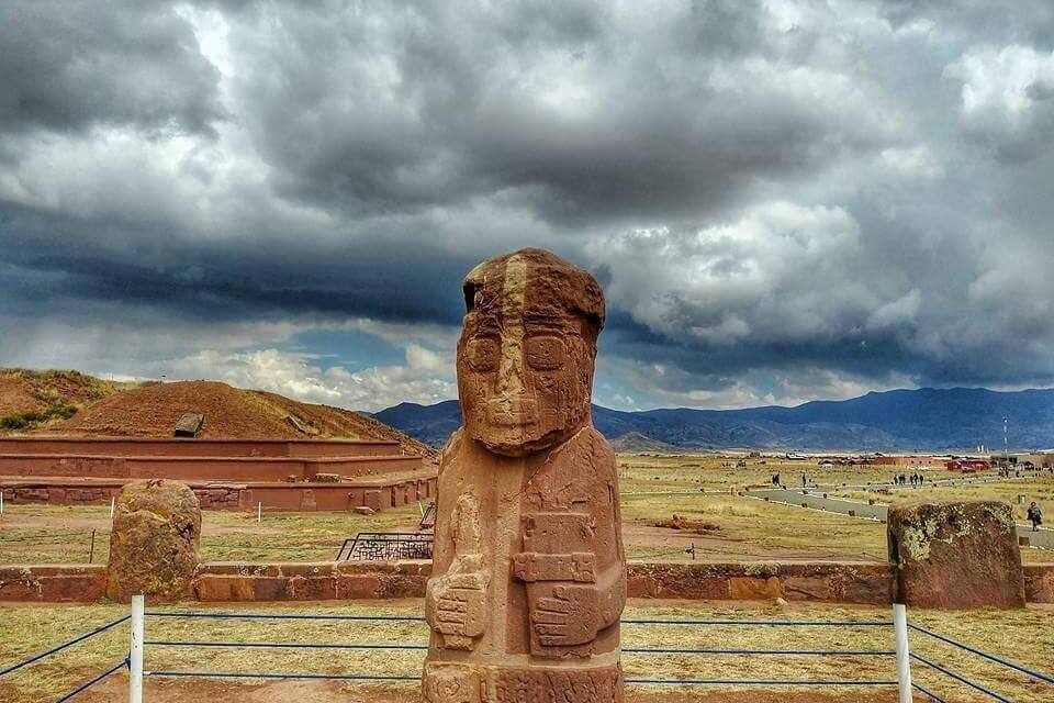 Uma estátua de pedra em um campo, com montanhas ao fundo.