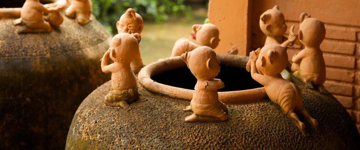 Terracotta figurines of children on large stone urns in a garden.