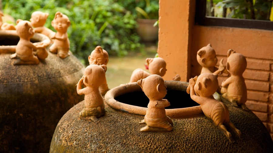 Petites figurines en terre cuite représentant des enfants, placées sur de grandes urnes en pierre dans un jardin.