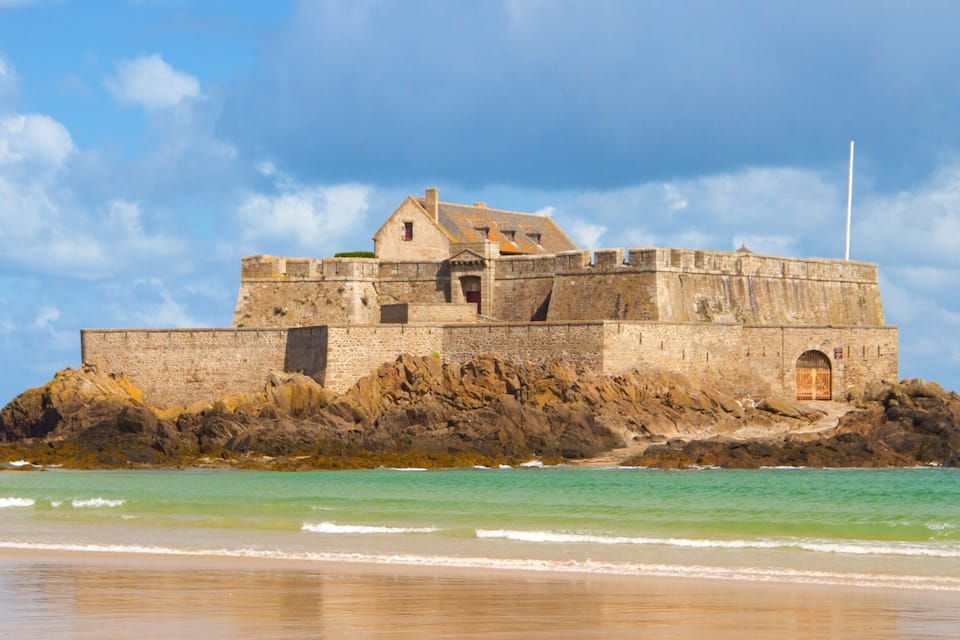 A historic stone castle on a rocky coastline with a clear sky.