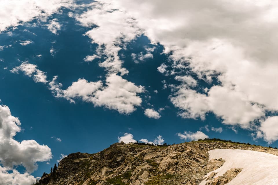 A mountain with a snow-covered peak and a clear blue sky with scattered clouds.