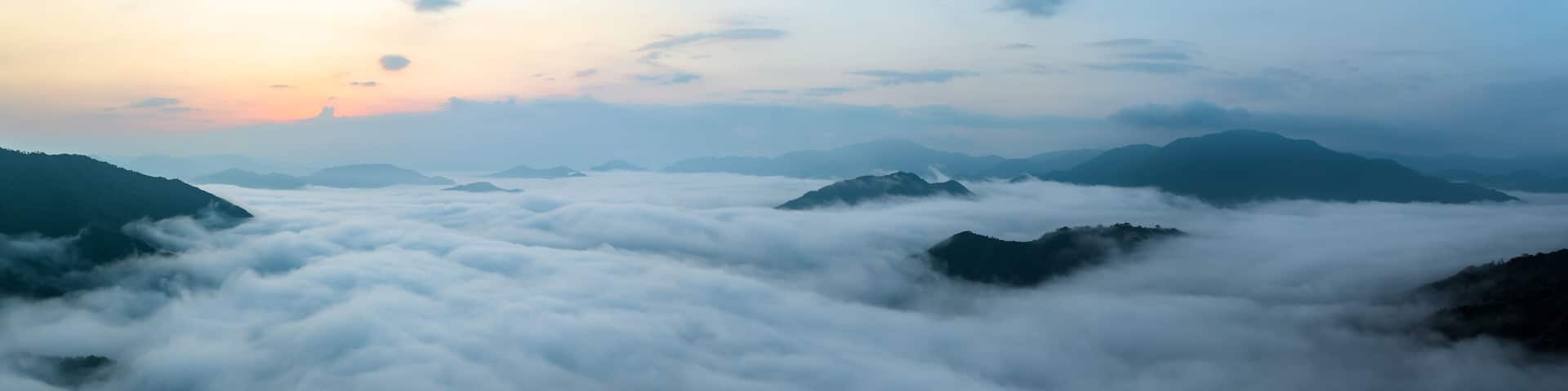 Panorama of sea of clouds around mountain peaks at sunrise