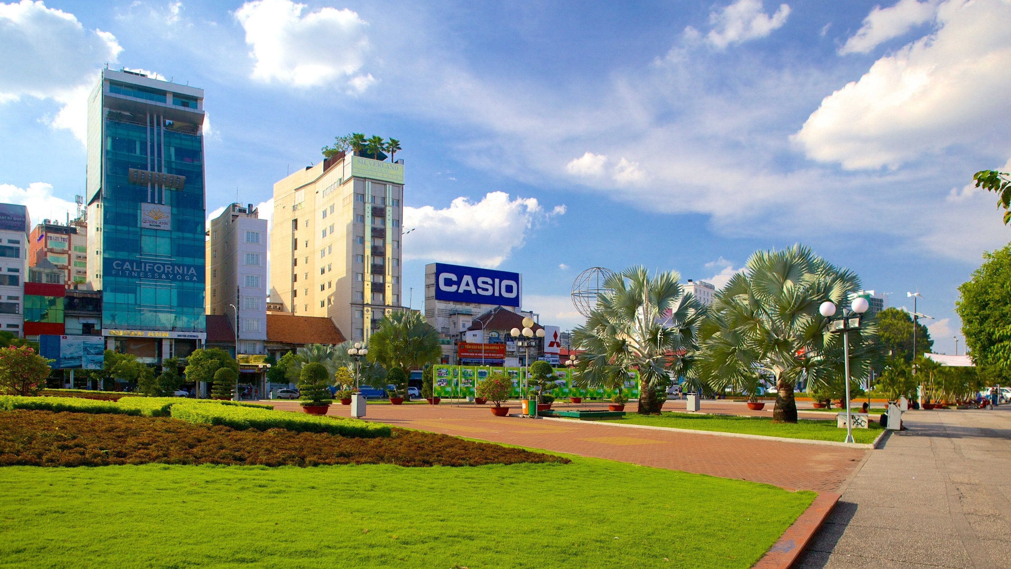Uma praça urbana com um letreiro Casio, um hotel Queen Ann e um centro de fitness.