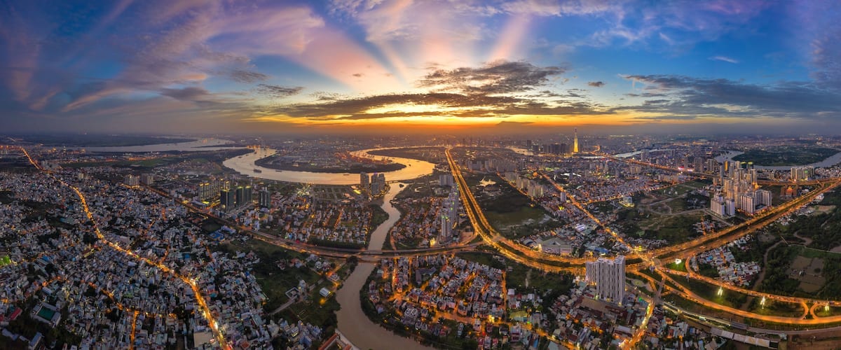 A panoramic view of a city at sunset with a river, bridges, and dense urban areas.