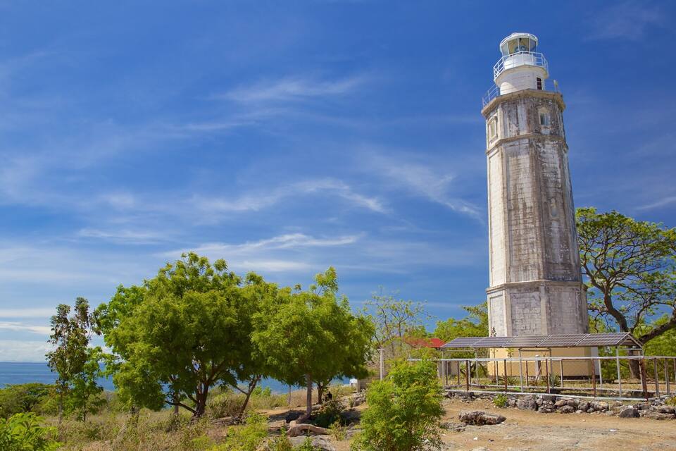 A tall lighthouse with a white top, surrounded by green trees and a clear blue sky.
