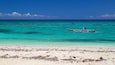 Una playa con aguas turquesas cristalinas y un bote con dos personas.