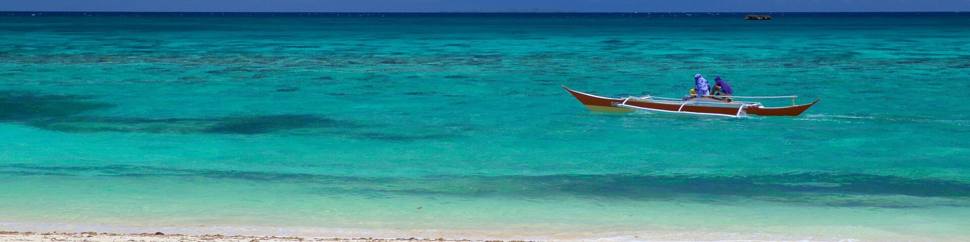 Una playa con aguas turquesas cristalinas y un bote con dos personas.