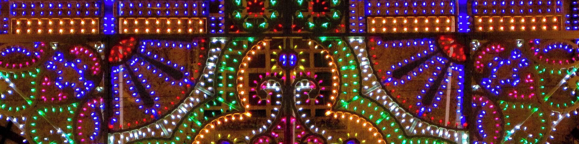 The "luminarie" (luminary) in Ortelle. Saint George and Saint Fortunato festival.
Everyone knows the Salento for its beautiful beaches and its views, for the goodness of local cuisine and the charm of its many traditions. But few may know that the Salento is also famous for many other aspects, which are revealed to visitors especially during the numerous festivities spread inland. We are talking about the incredible interplay of light of the illuminations, also called villas: these little colored lights which cover entire buildings as waterfalls, churches, streets and squares, forming unique settings can keep their eyes upward everyone from the largest to the smallest.