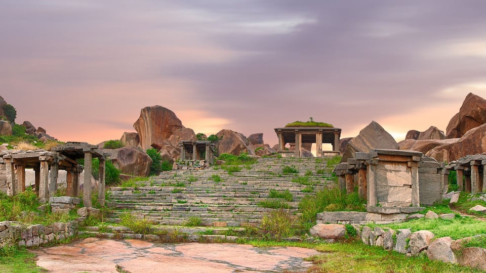 Ancient stone ruins with stepped pathways and columns, surrounded by large boulders and greenery.