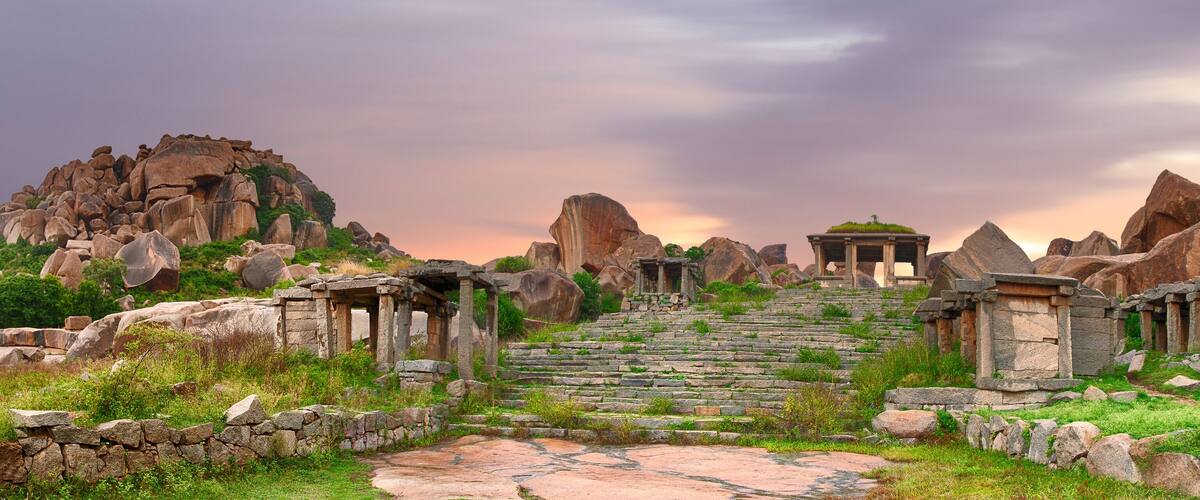 Ancient stone ruins with stepped pathways and columns, surrounded by large boulders and greenery.
