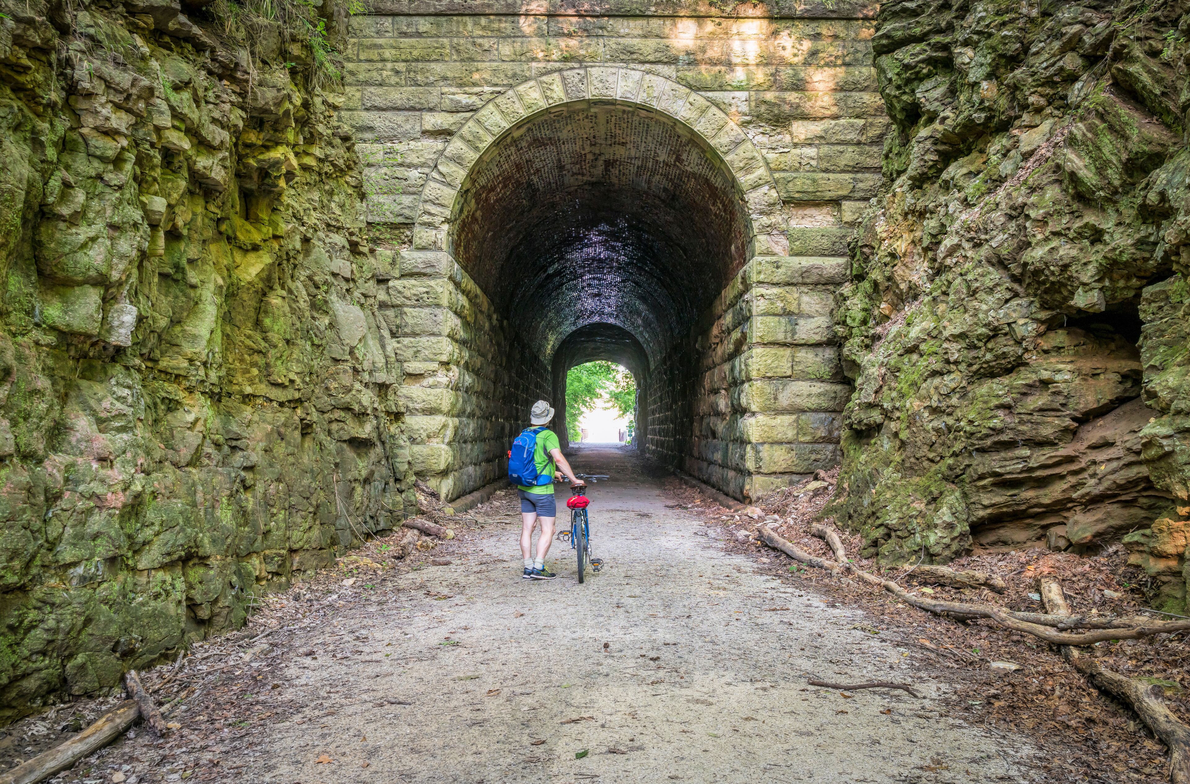 A person on a bicycle in a stone tunnel with moss-covered walls.