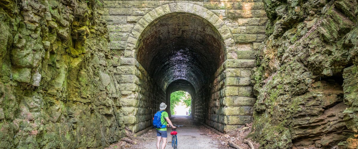 A person on a bicycle in a stone tunnel with moss-covered walls.