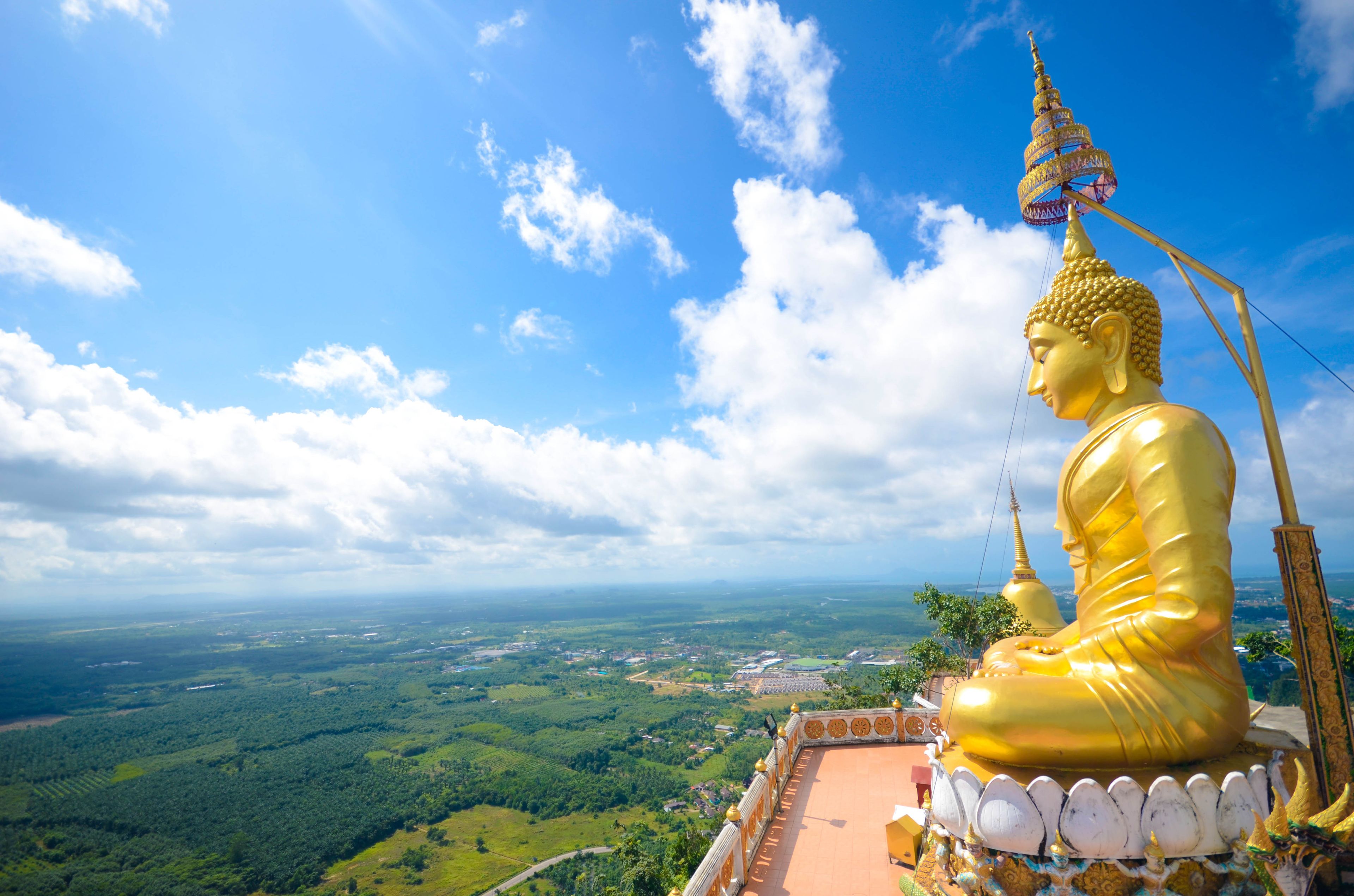 A golden Buddha statue overlooking a landscape with a clear sky.