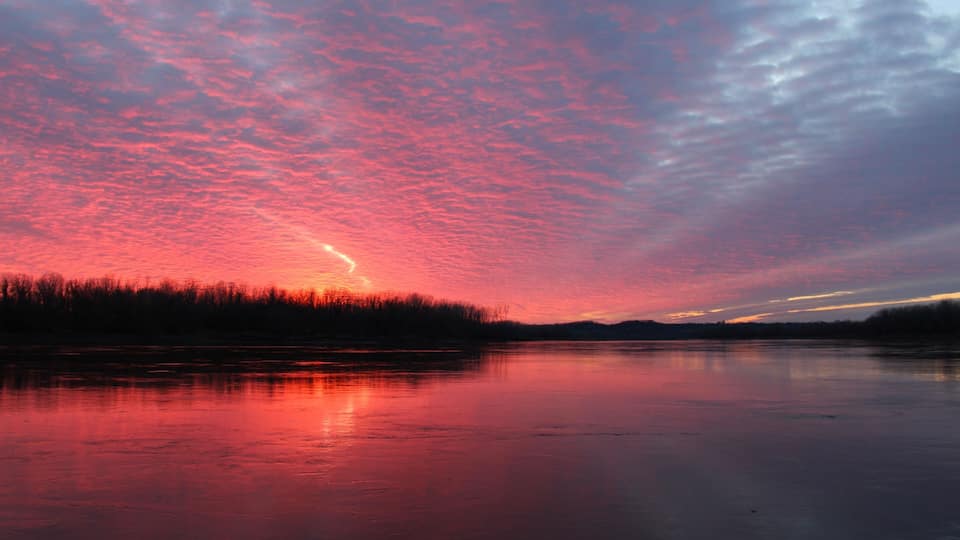 A frozen lake with a sunset and a forest in the background.