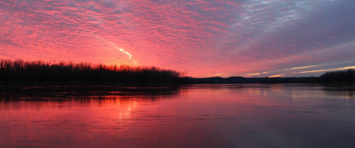 A frozen lake with a sunset and a forest in the background.