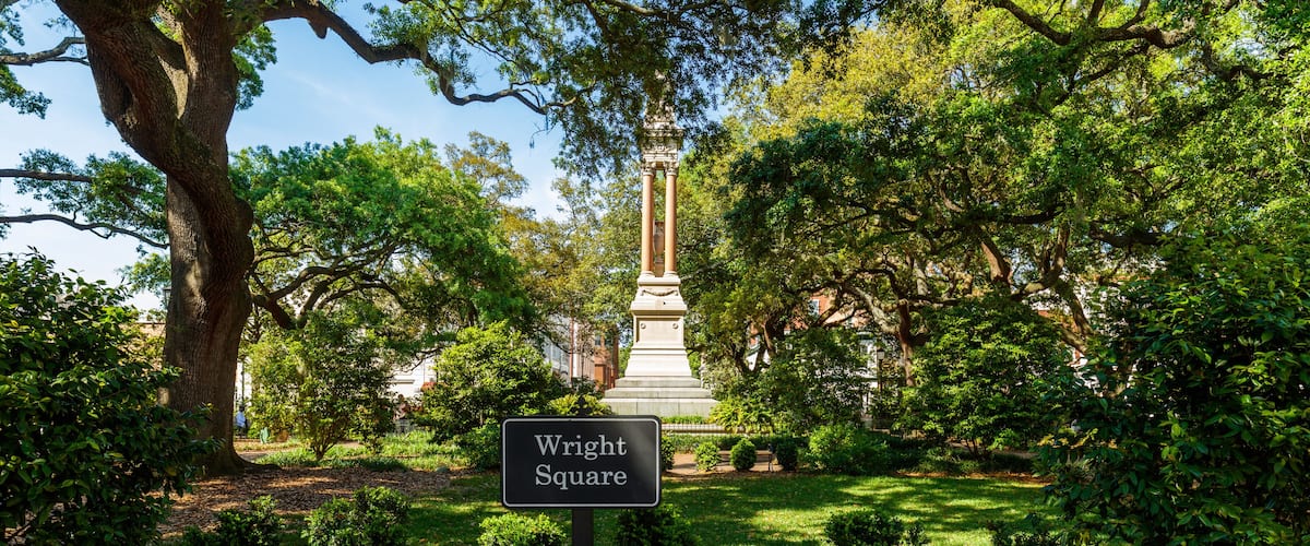 A park with a monument, a sign reading "Wright Square," and lush greenery.