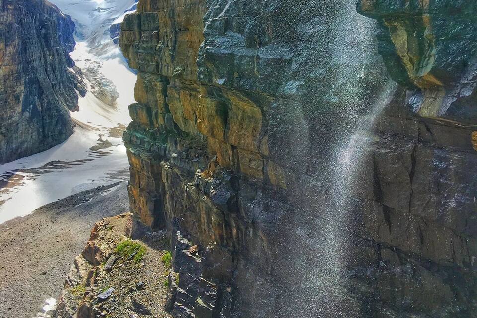 A waterfall cascading down a rocky cliff with a glacier in the background.