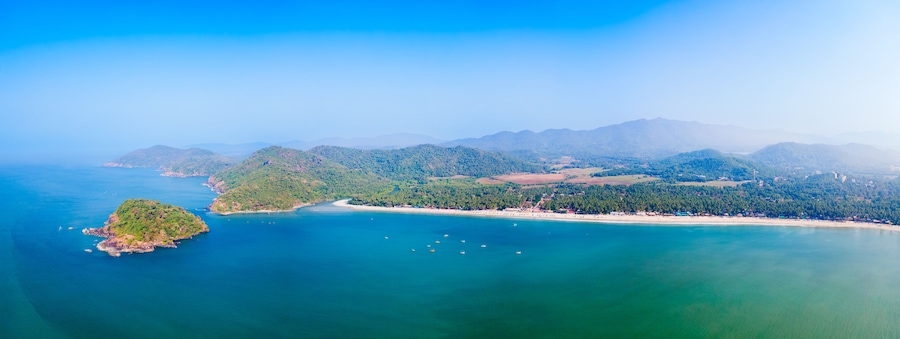 Vista aérea de una región costera con una pequeña isla, una playa y un paisaje montañoso.