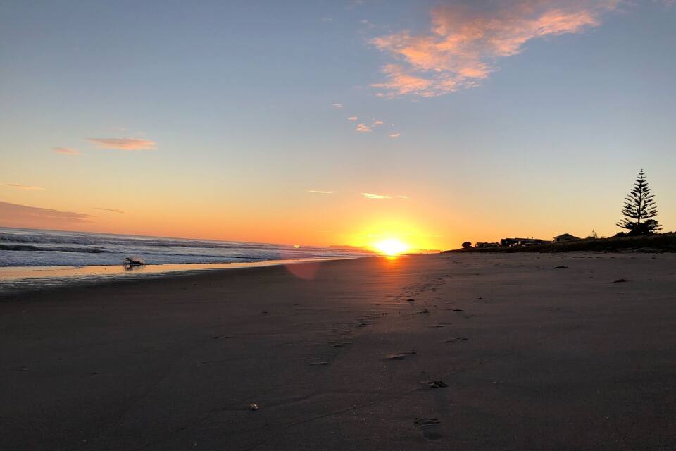 A beach at sunset with the sun low on the horizon, waves gently lapping the shore, and footprints in the sand.