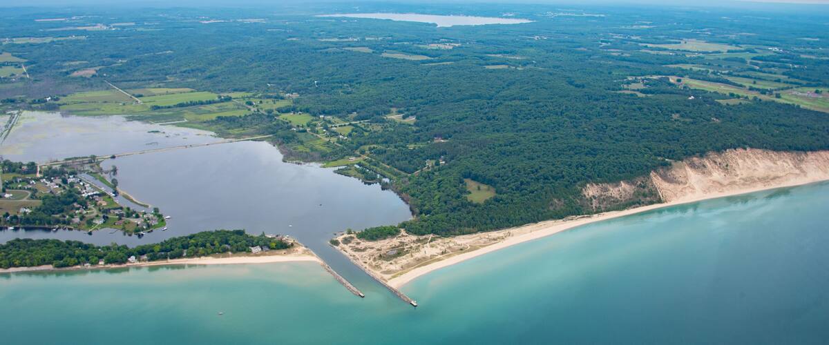 An aerial view of a coastal area with a large body of water, a sandy beach, and a forested region.