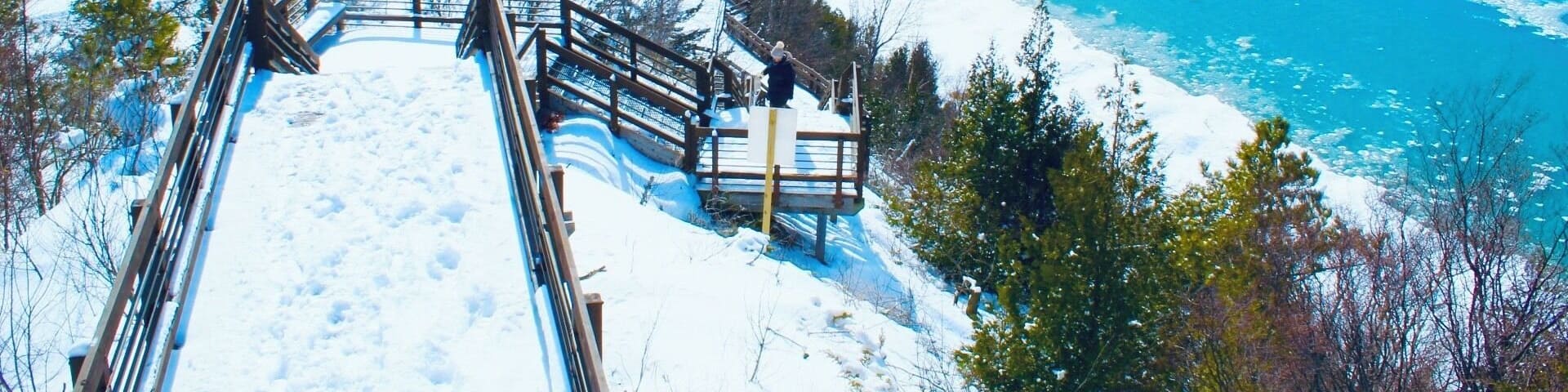 A snow-covered wooden staircase leading down to a frozen lake.