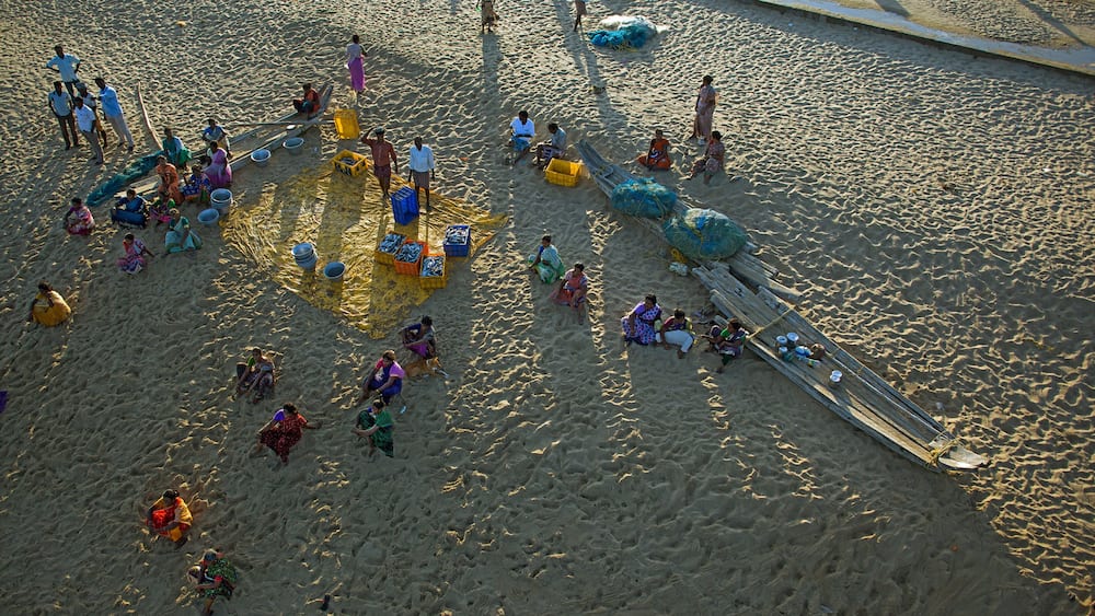 Une plage de sable où l’on voit des gens, des bateaux et des conteneurs aux couleurs vives.
