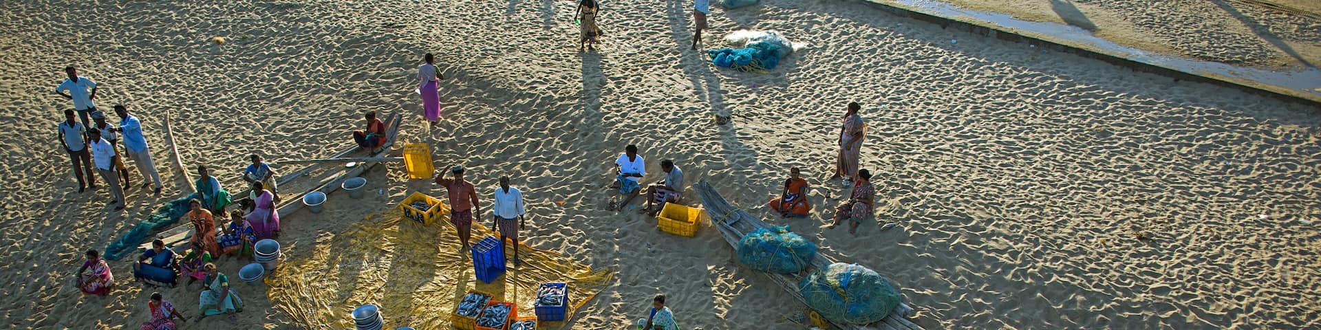 A sandy beach with people, boats, and colorful containers.