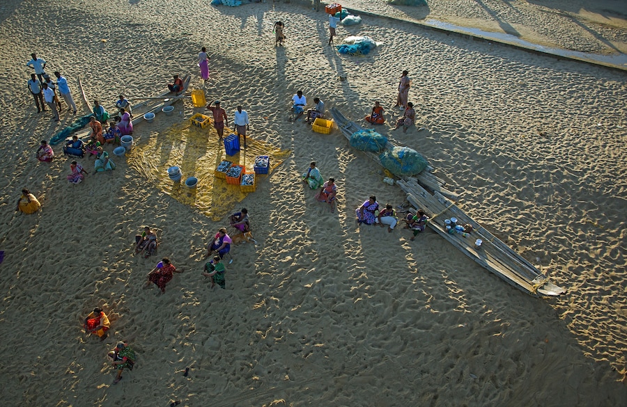 A sandy beach with people, boats, and colorful containers.