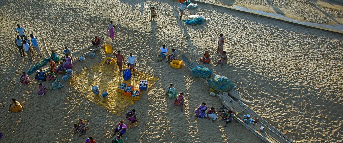 A sandy beach with people, boats, and colorful containers.