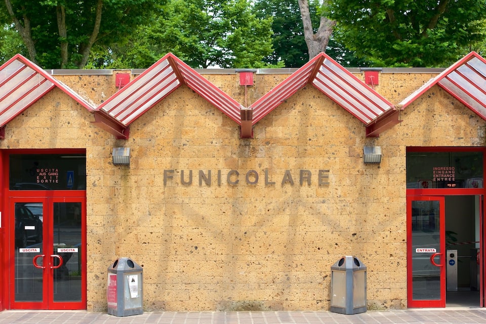 Un edificio con un letrero que dice "FUNICOLARE" y puertas rojas con letreros que indican "USCITA".