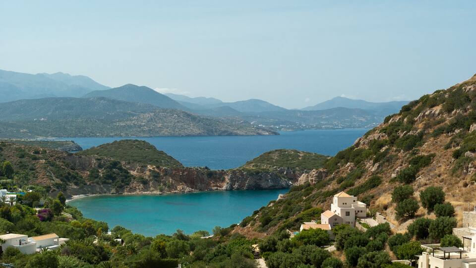A coastal landscape with a turquoise bay, green hills, and white buildings.