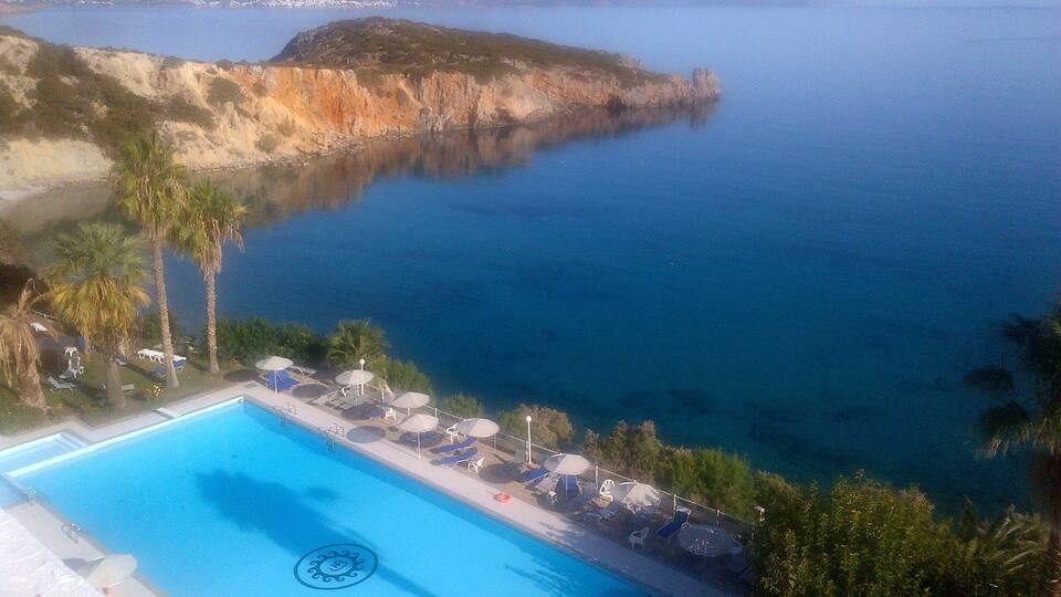 A pool with lounge chairs and umbrellas, overlooking a coastal area with cliffs and a body of water.