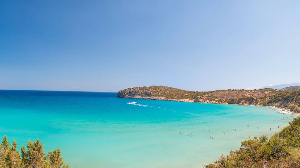 A turquoise sea, sandy beach, rocky coastline, and green hills.