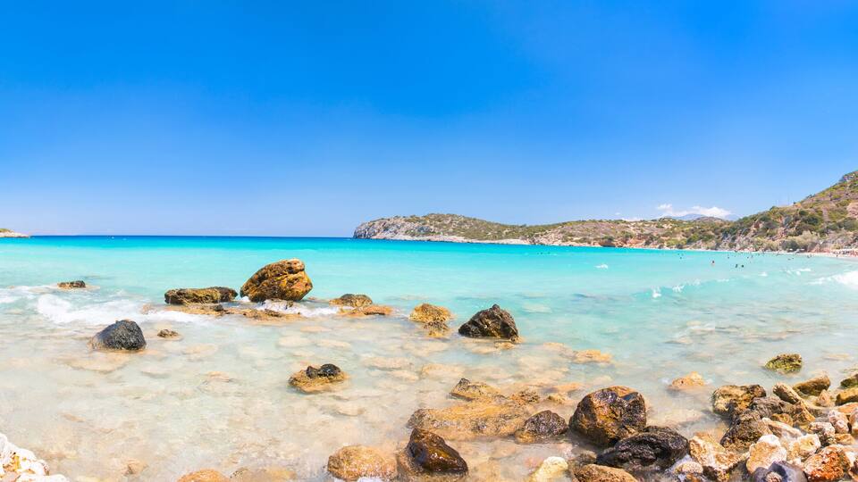 A rocky beach with clear turquoise waters and distant hills.