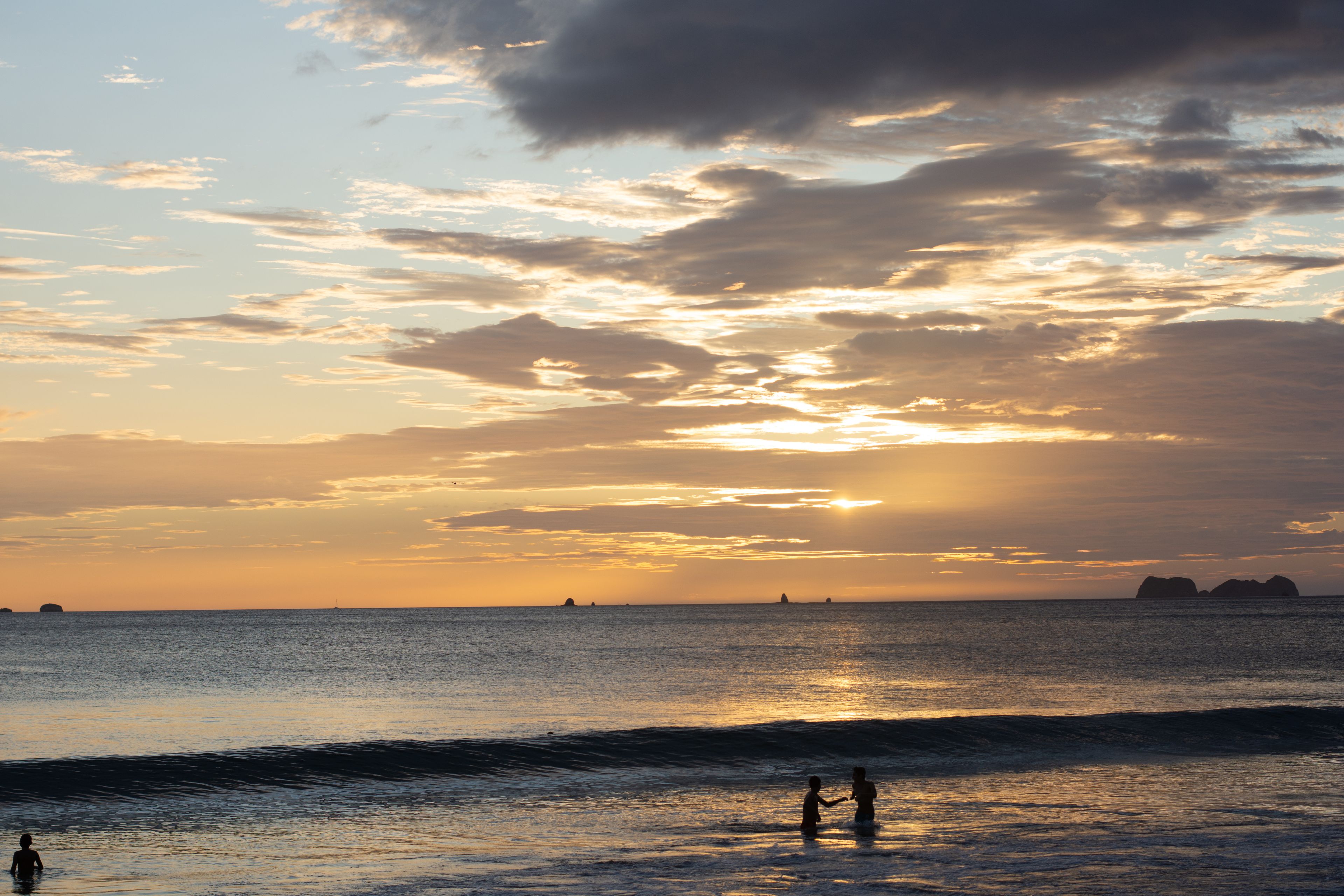 A sunset over a calm sea with silhouettes of people and distant islands.