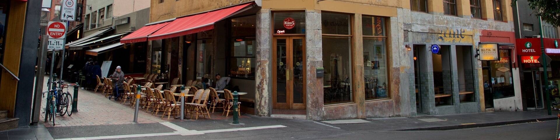 A street corner with a yellow building, outdoor seating, and a red awning.