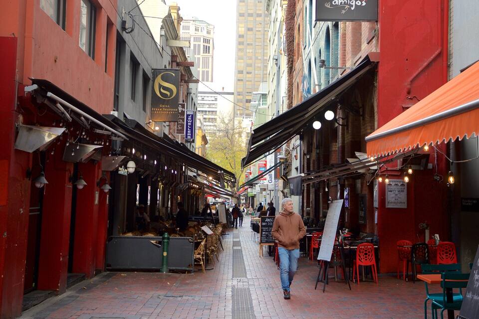 A narrow street lined with restaurants and shops, featuring a red brick pavement and a mix of red and white buildings.