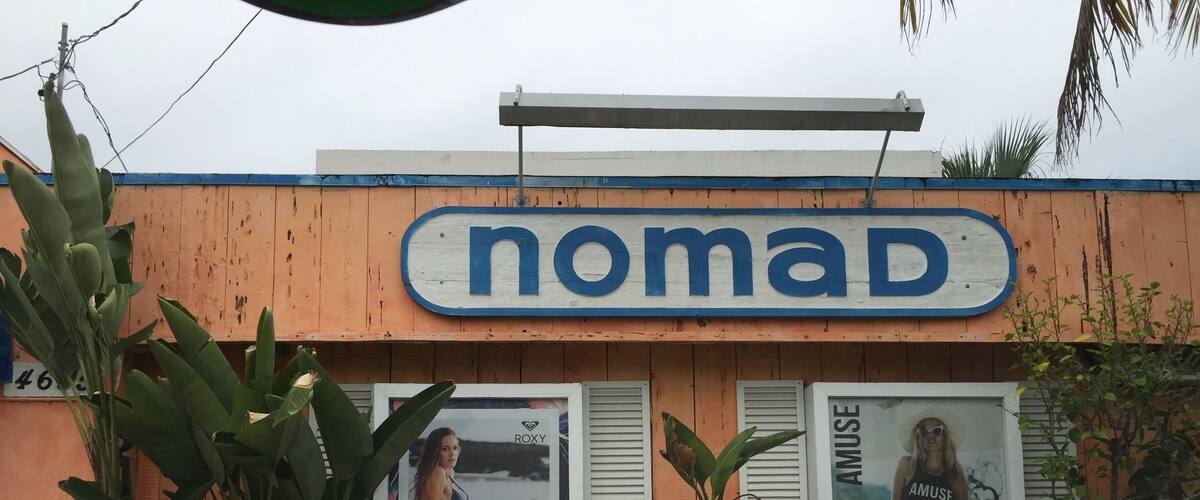 A storefront with the sign "nomad" and two advertisements for Roxy and Amuse.