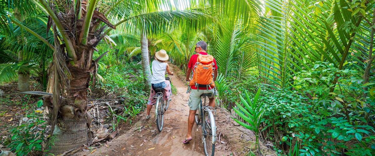 Two people on bicycles in a dense tropical forest with palm trees.