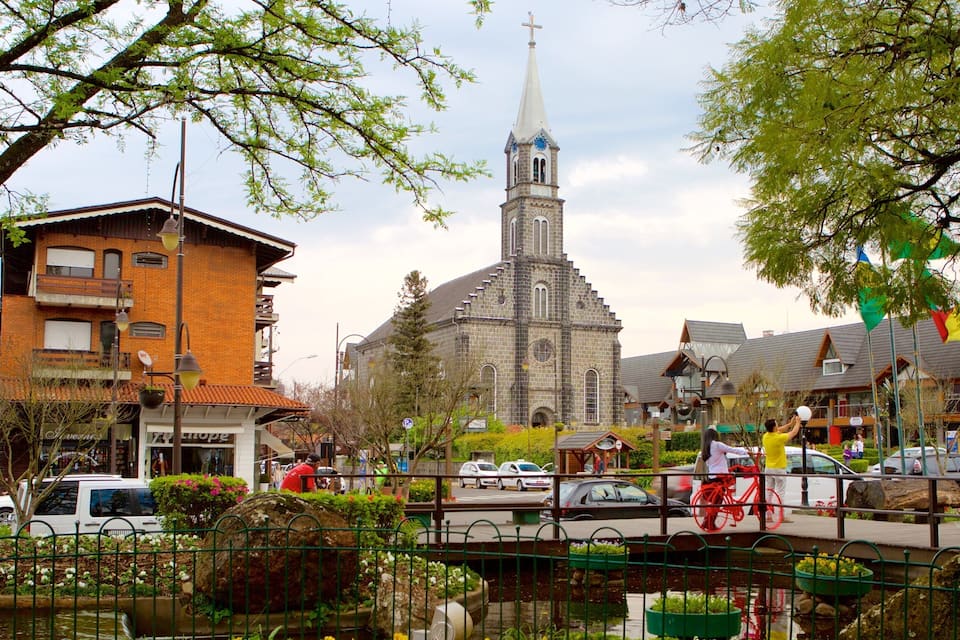 Une église avec un clocher imposant, un bâtiment en briques avec une enseigne, et une rue où l’on voit des voitures et un vélo.